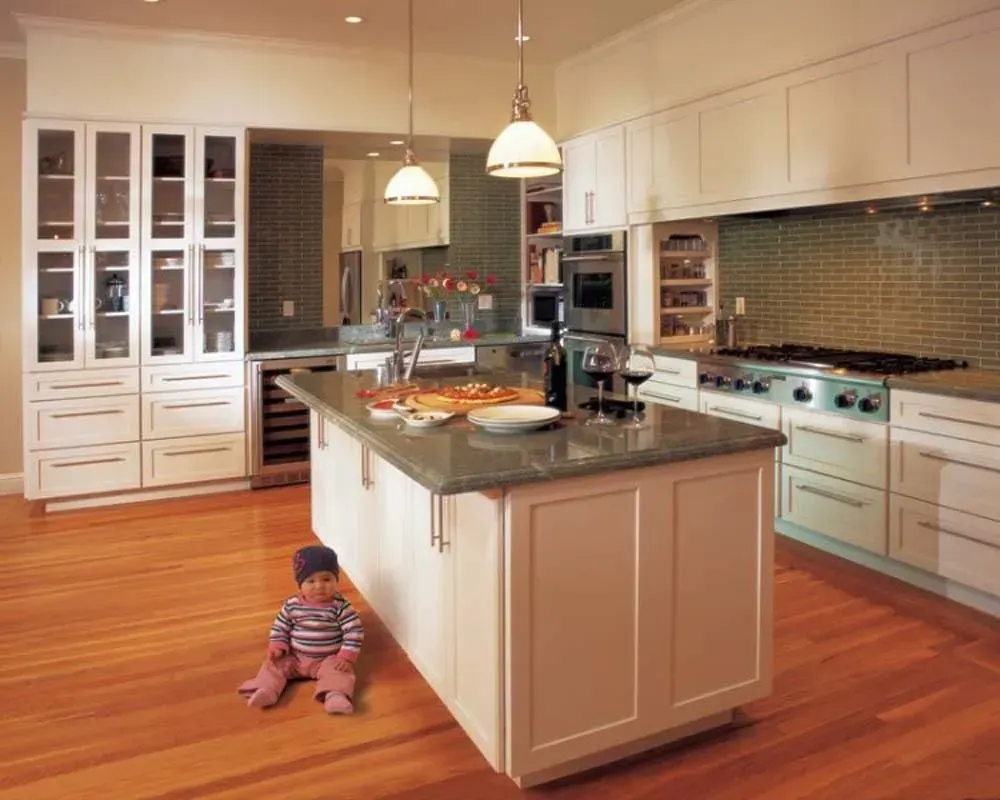 Bright kitchen with island, white cabinets, hardwood floor, and a small child sitting near the island.