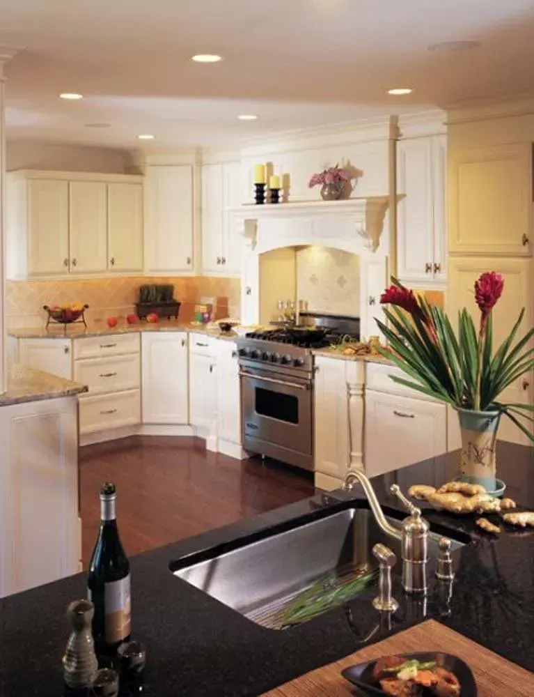 Bright white kitchen with stainless stove, dark countertops, and a vase of pink flowers on the island