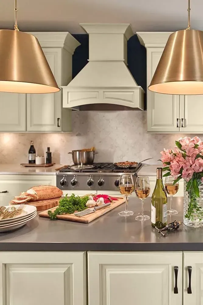 Elegant kitchen with cream cabinets, stainless stove, marble island, pastries, and pink flowers.