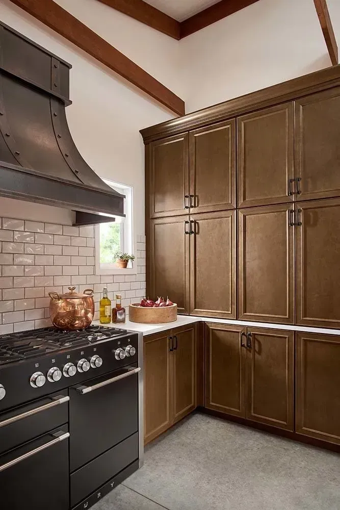 Modern kitchen with black stove, white tile backsplash, and tall wooden cabinets under exposed beams