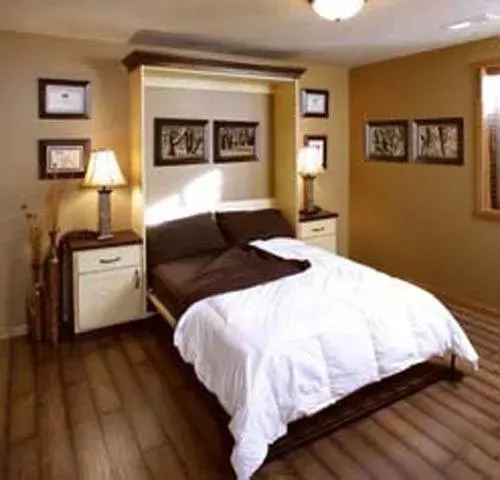 Cozy bedroom with a neatly made bed, warm lighting, wood floors, and framed wall art