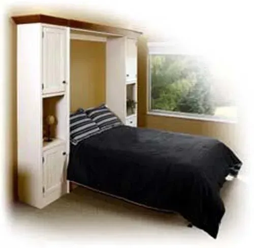 Wall bed with black bedding built into white cabinets beside a large window.