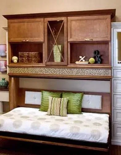 Wooden wall bed with cabinets and shelves, made up as a seating area with green and striped pillows.