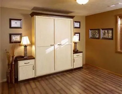Warm-toned room with a white wardrobe, two bedside tables, lamps, framed art, and striped wood flooring