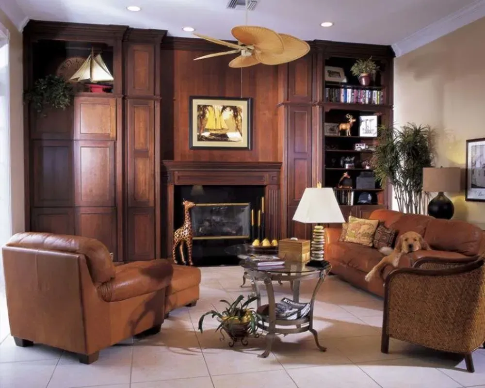 Elegant living room with wood-paneled fireplace, leather chairs, patterned sofa, and lamp on a glass coffee table