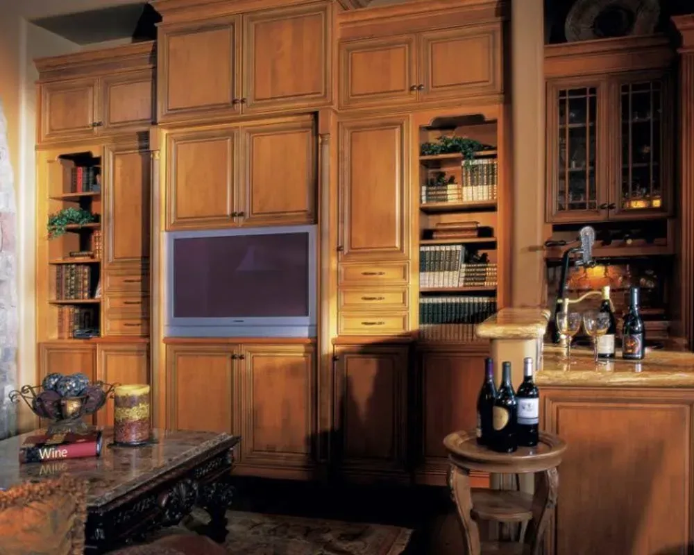 Wood-paneled kitchen wall with built-in cabinets, shelves, and a small TV above a countertop and table.