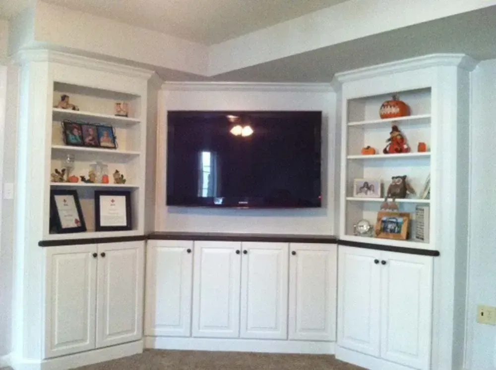 White built-in corner entertainment center with TV, shelves, cabinets, and decorative items