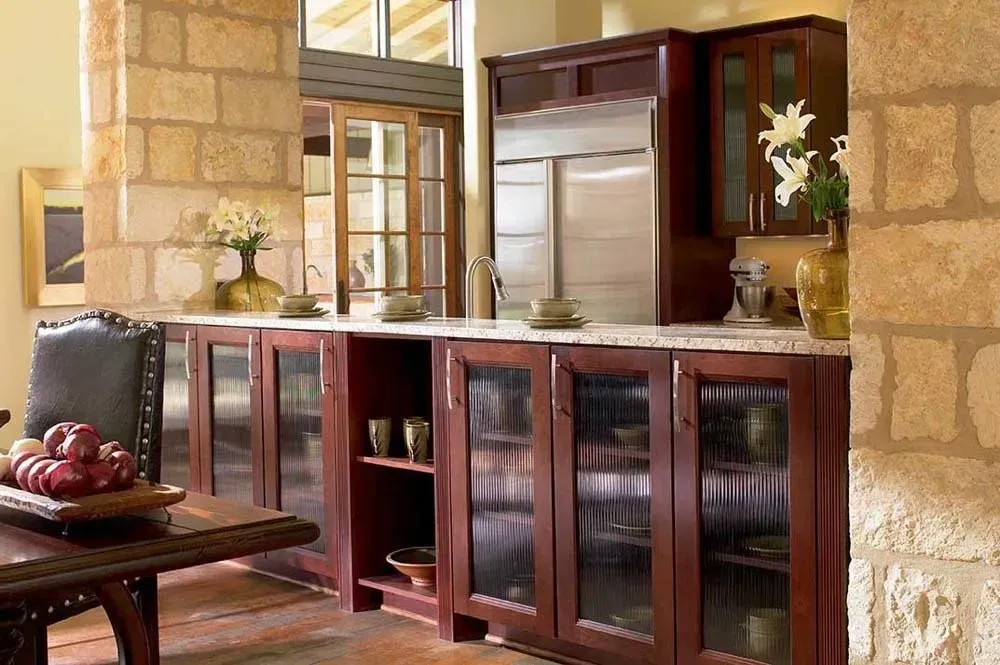 Stone-walled kitchen with wooden cabinets, granite counter, and glass doors in a warm interior