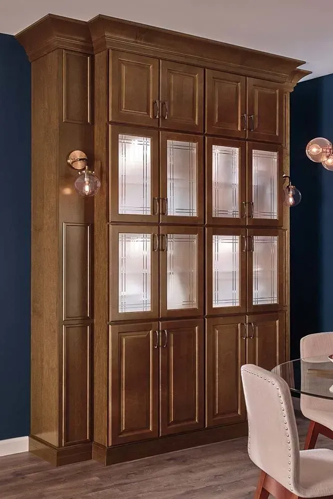 Tall wooden built-in cabinet with glass-paneled doors in a dining room beside a table and chairs