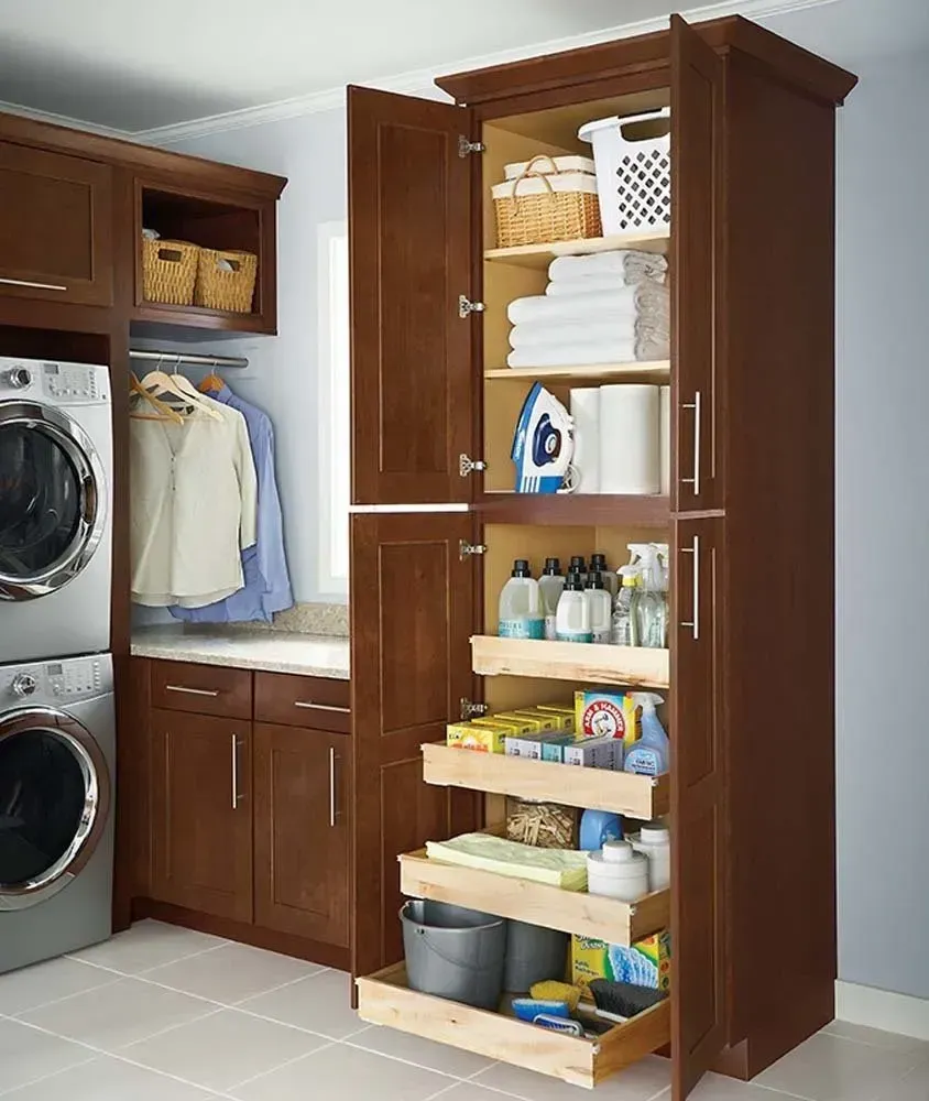 Laundry room with tall brown storage cabinets, folded towels, ironing board, and washer-dryer stack