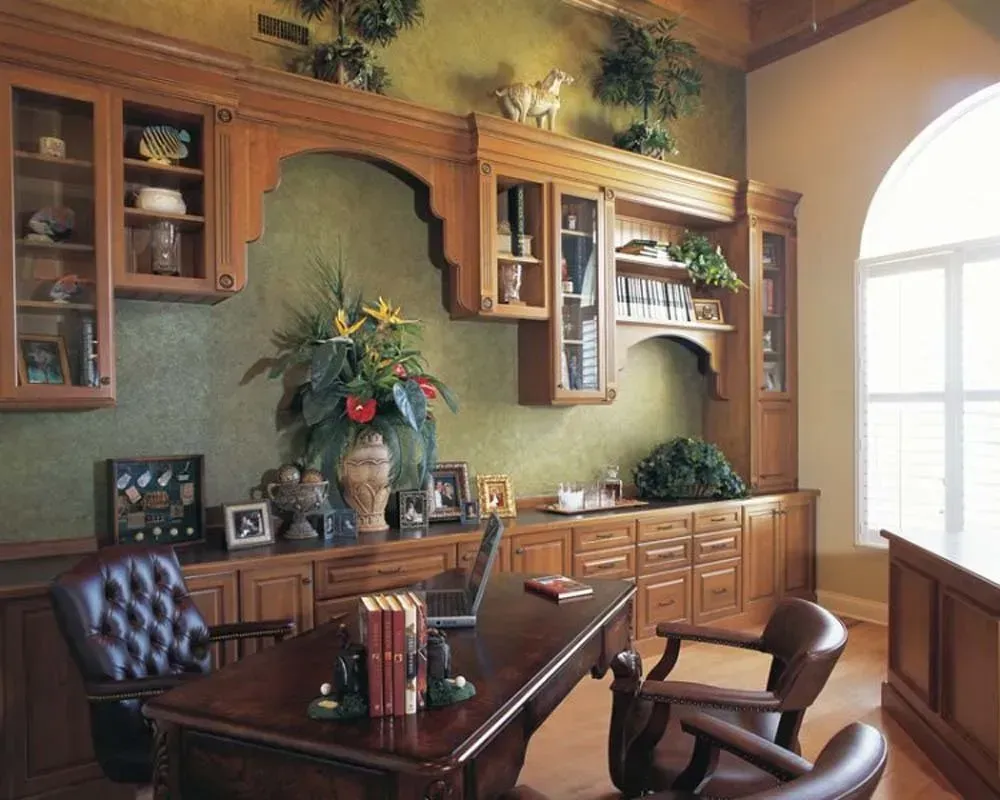Elegant home office with wood cabinets, dark desk, and large arched window.