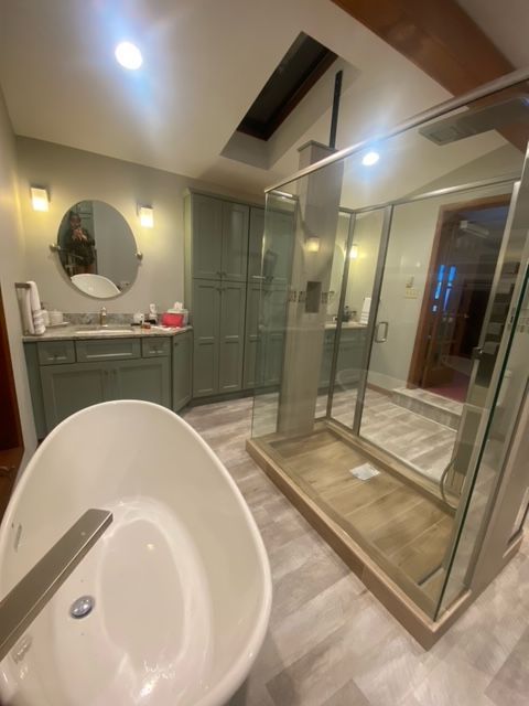 Modern bathroom with white tub, glass shower enclosure, and gray vanity with round mirror
