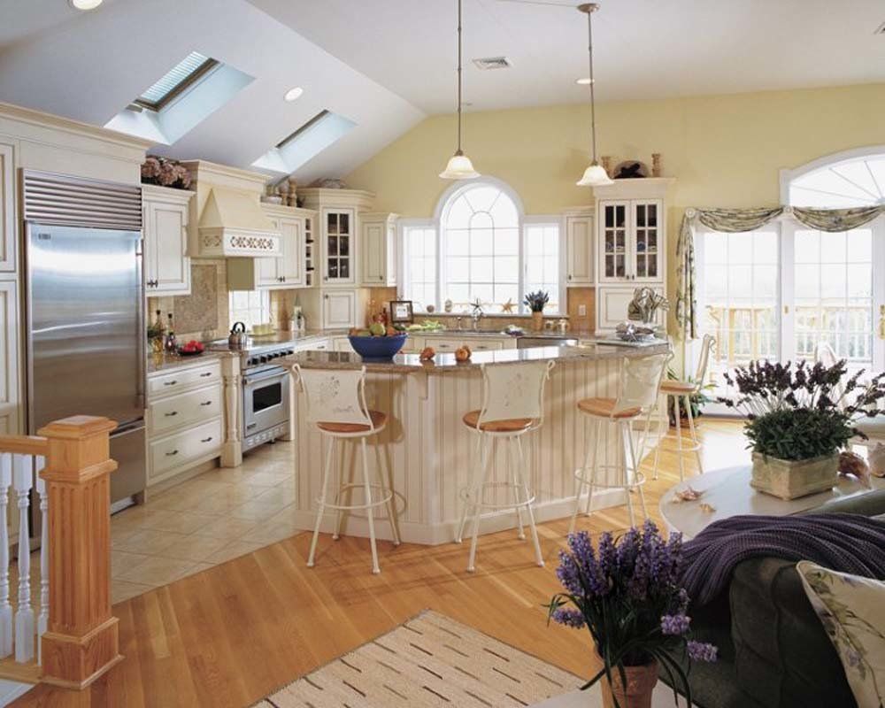 Bright white kitchen with island, bar stools, skylights, and wood floors, decorated with flowers.