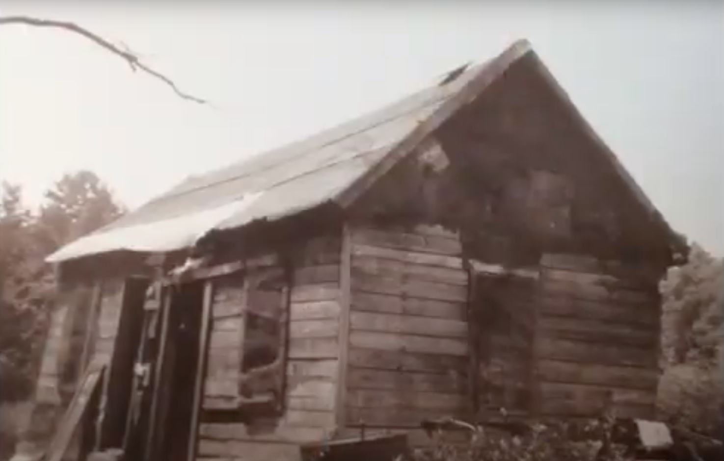 A black and white photo of a small wooden house with a tin roof.
