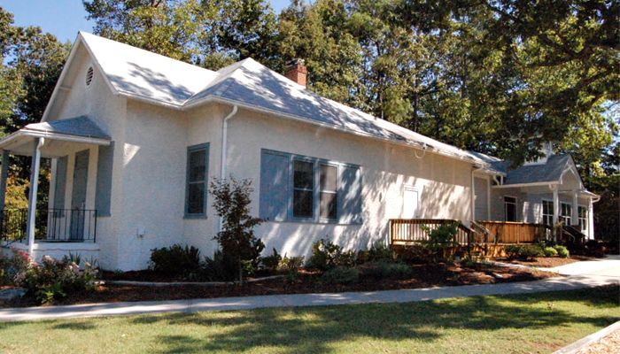 A white house with blue shutters is surrounded by trees