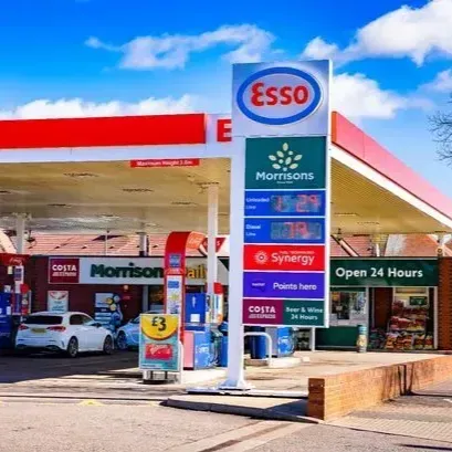 Esso gas station with a Morrison's store, under a red awning, and a price sign against a blue sky.
