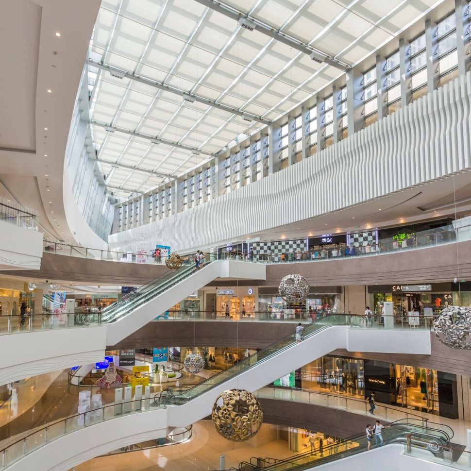 Multi-level shopping mall with escalators, stores, and glass roof.