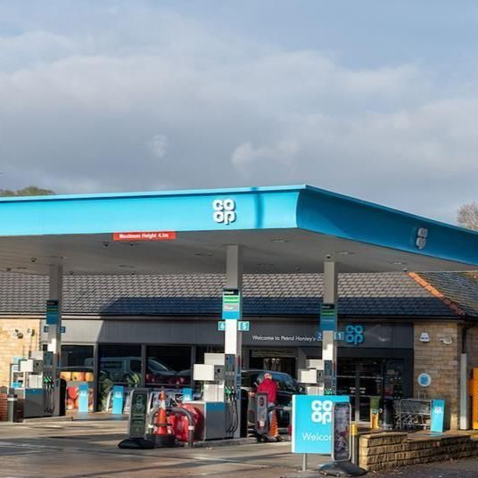 Co-op gas station with blue canopy; people, cars, pumps. Building of brick and stone.