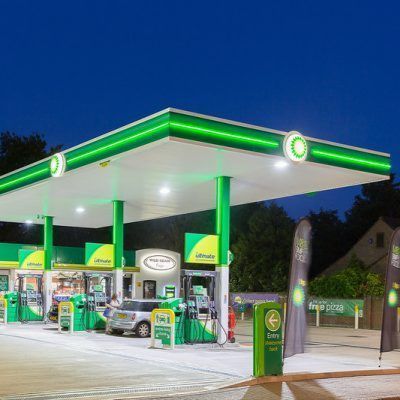 BP gas station with green and white branding at dusk; fuel pumps, car, signage.