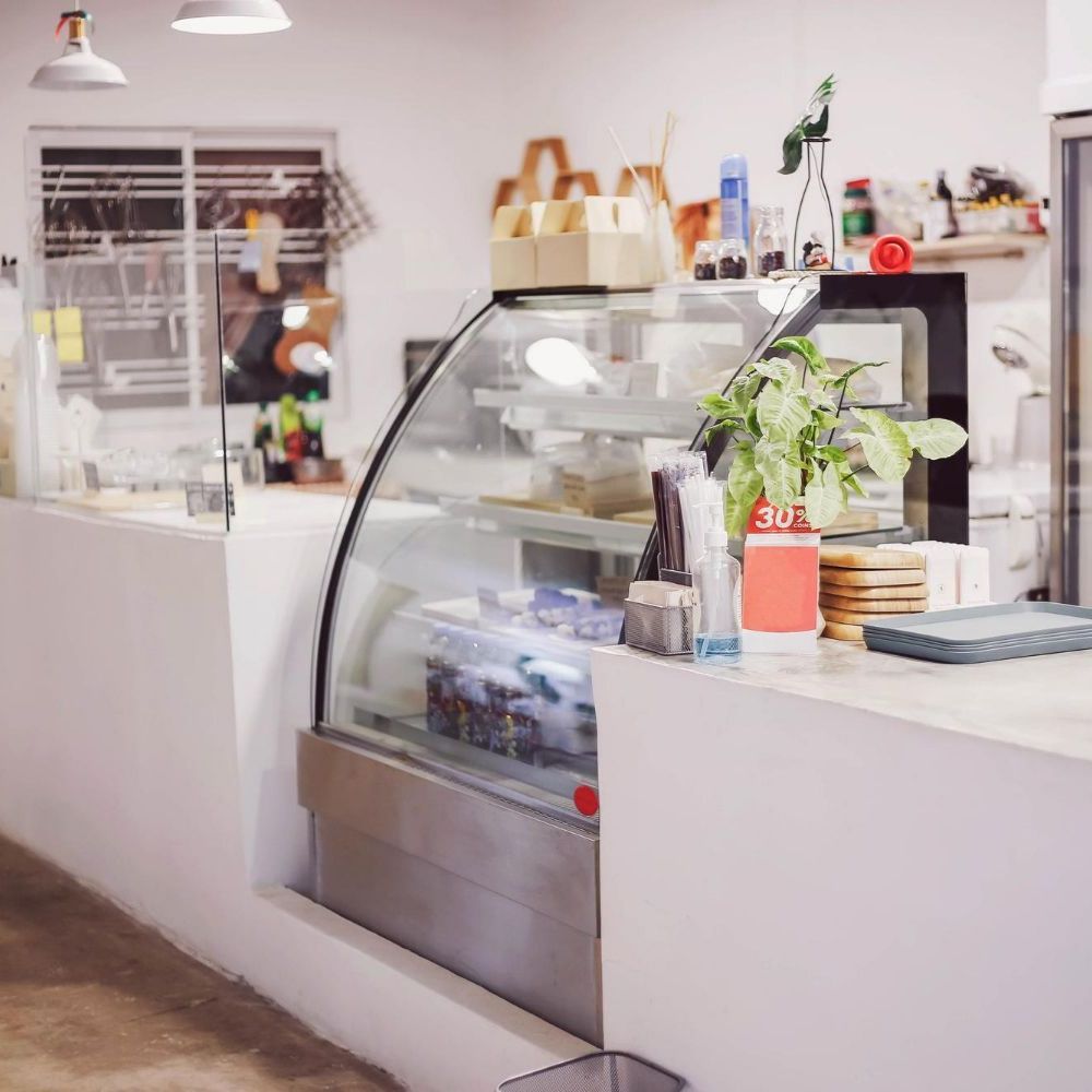 Interior view of a cafe with a white counter, display case, and various products.