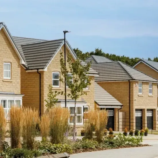 Row of new beige houses with grey roofs, blue sky. Landscaping in foreground.