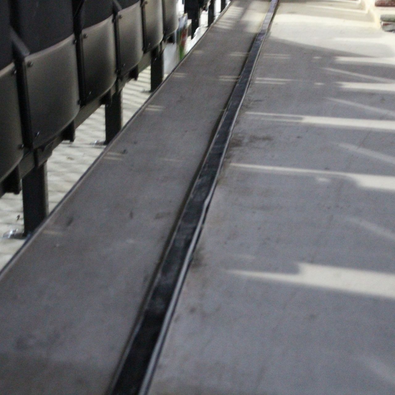 Long, narrow, dark gutter along a concrete surface near bleacher seating.