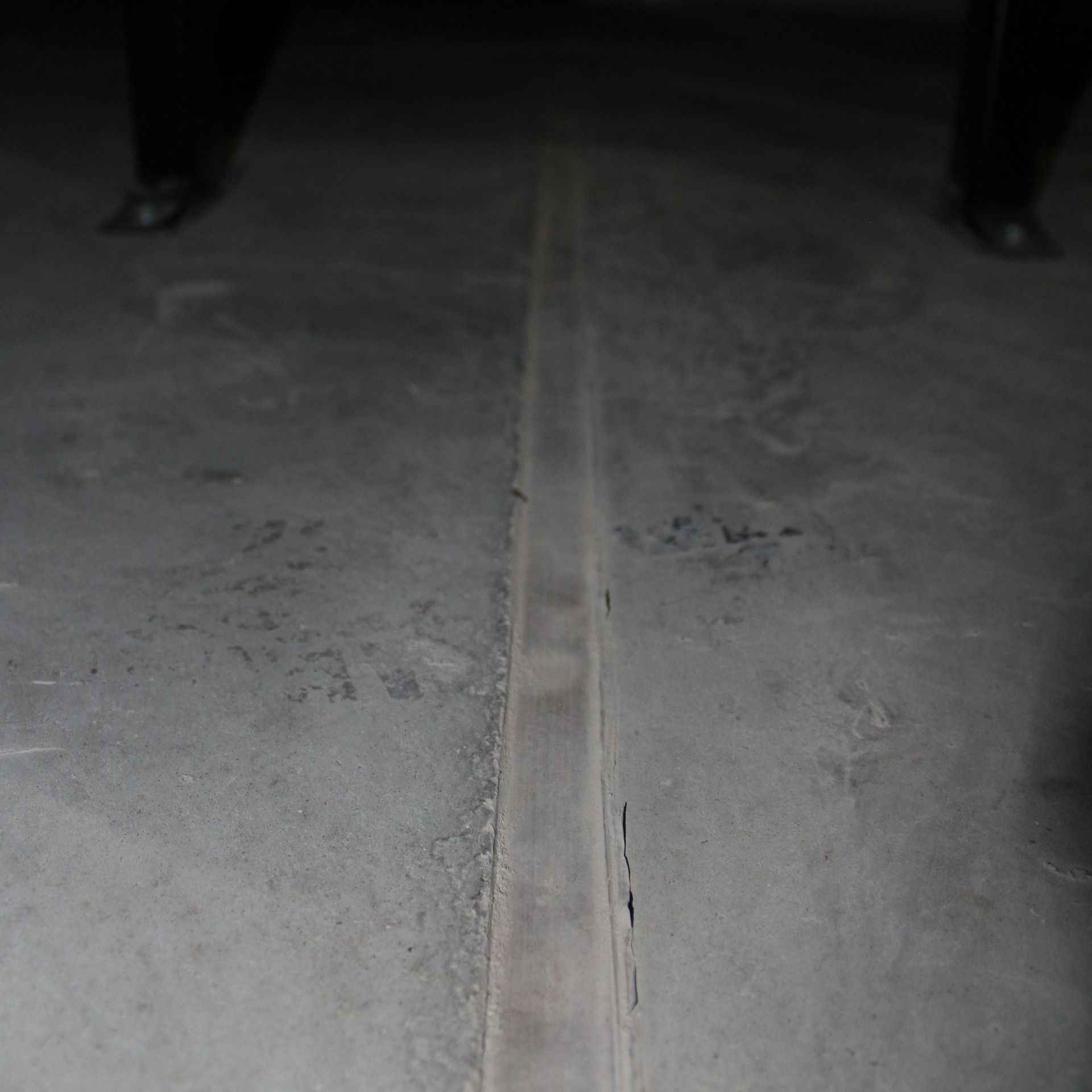 Concrete floor with a dark crack running down the center, flanked by two pairs of feet.