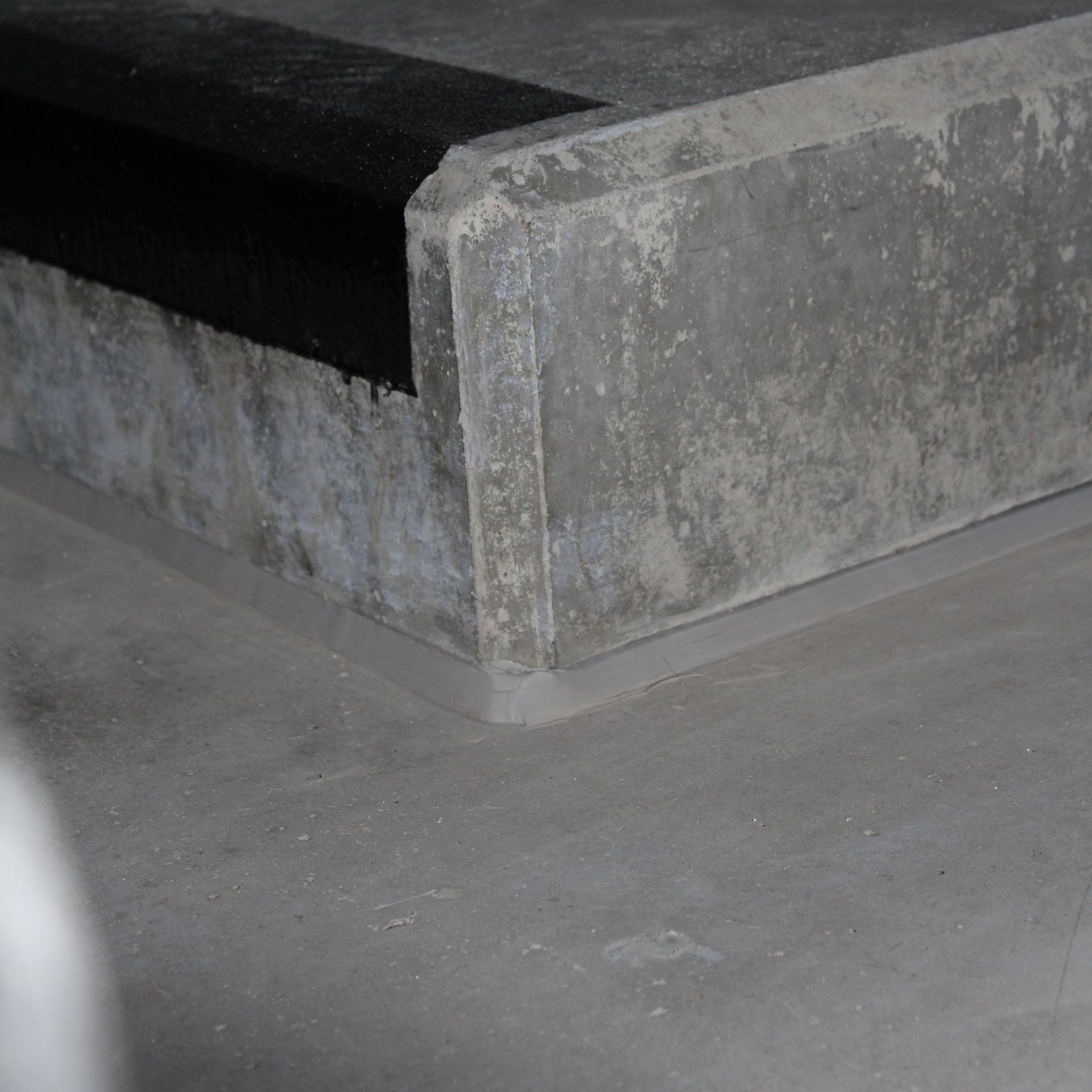 Corner of a concrete structure with a black rubber strip at the top edge and a light-colored floor.