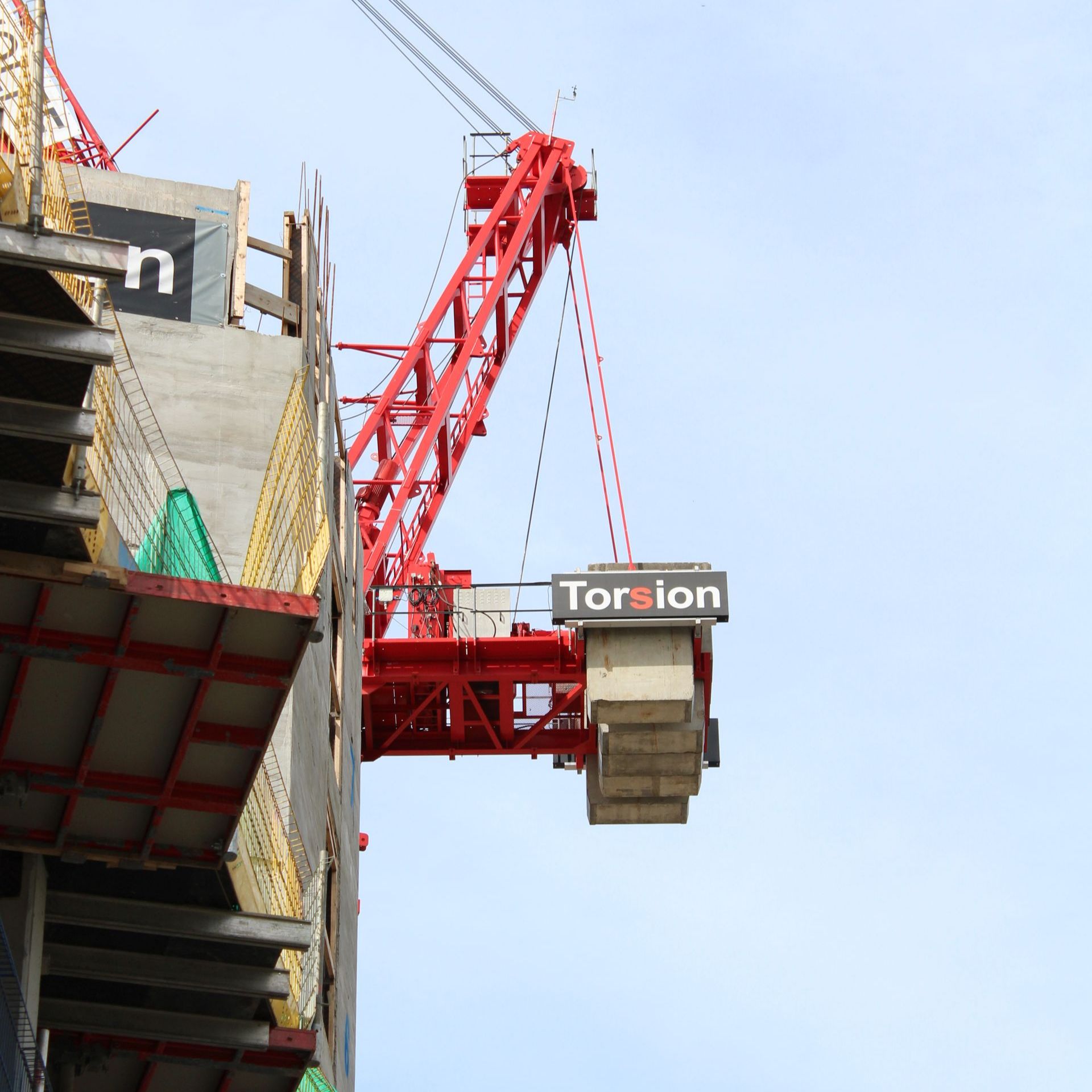 Construction crane, red, lifting materials at building site, gray concrete structure, blue sky background.