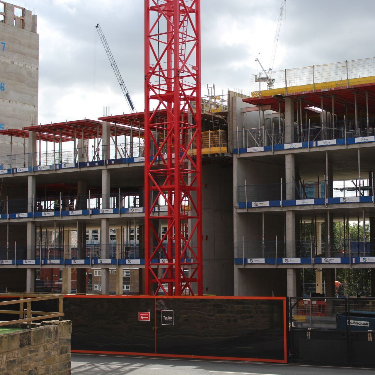 Construction site with red crane, building under construction, and safety barriers.