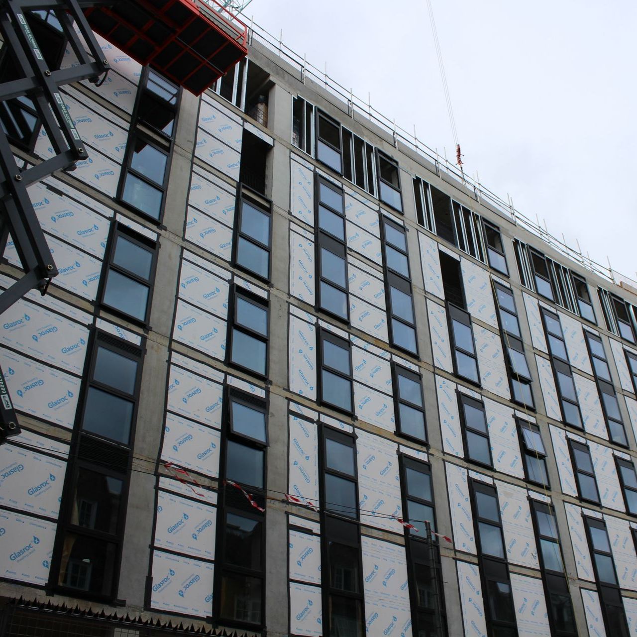 Construction site with a multi-story building; windows installed, white panels on exterior; overcast sky.