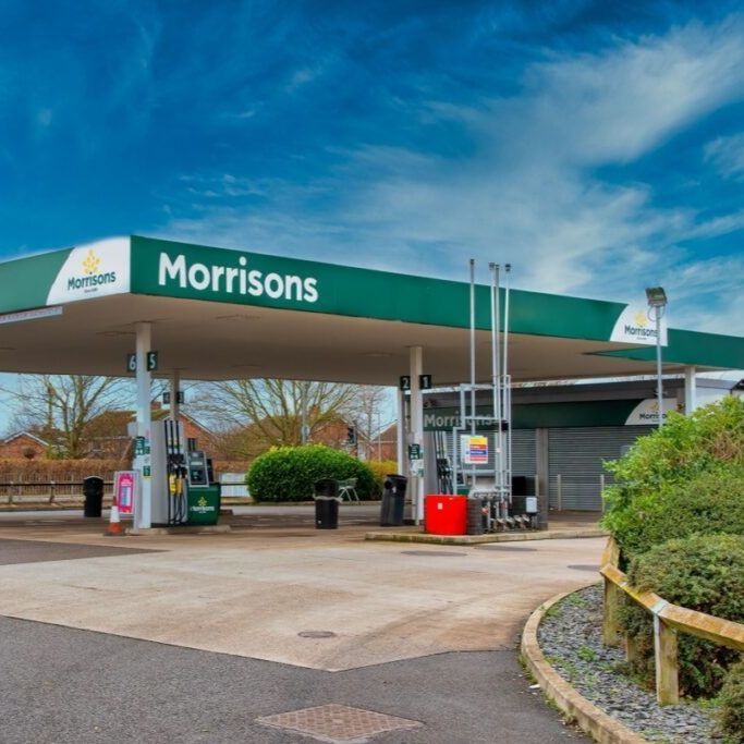 Morrisons petrol station under a bright blue sky; green canopy over pumps.
