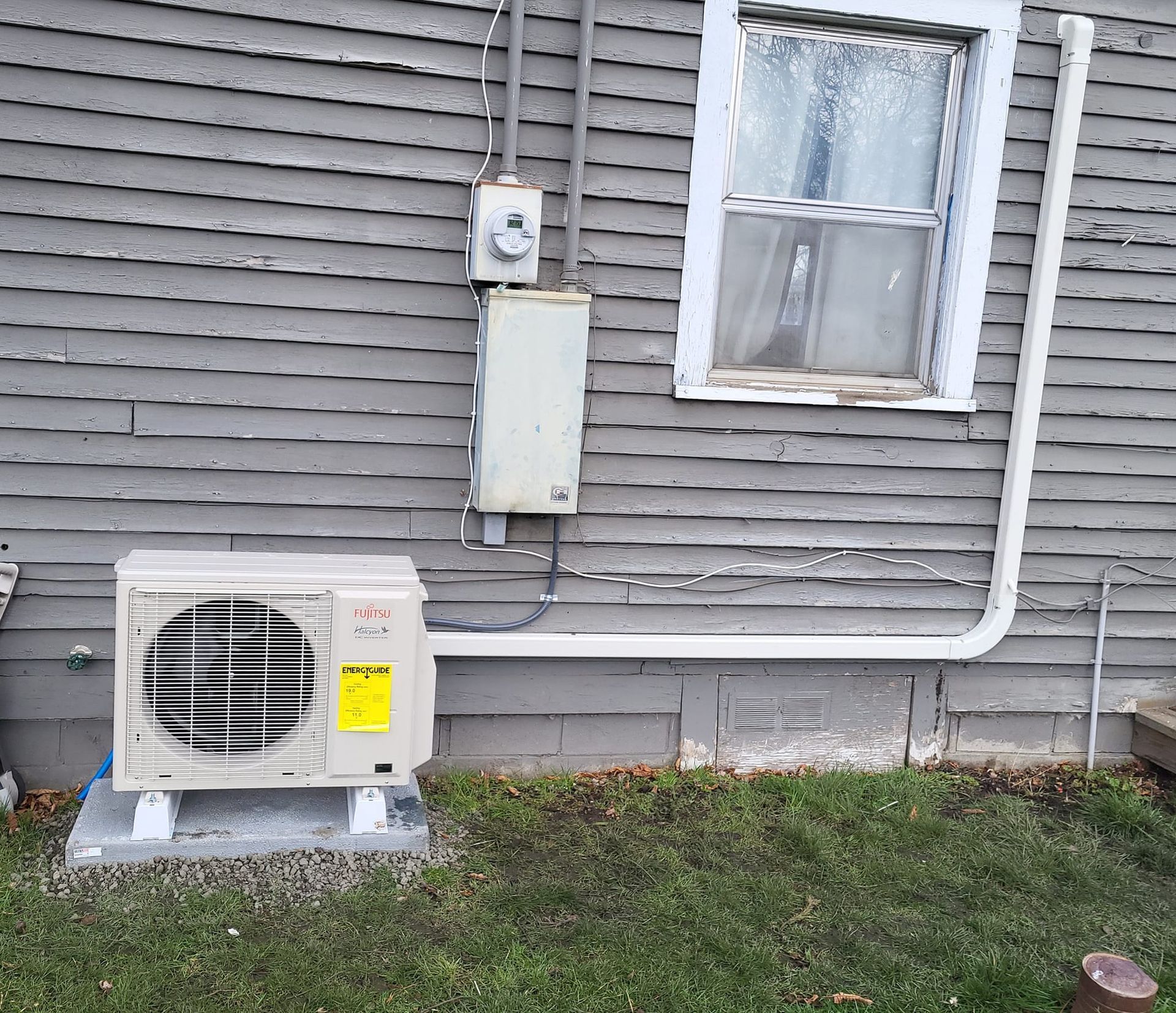 An air conditioner is installed on the side of a house next to a window.