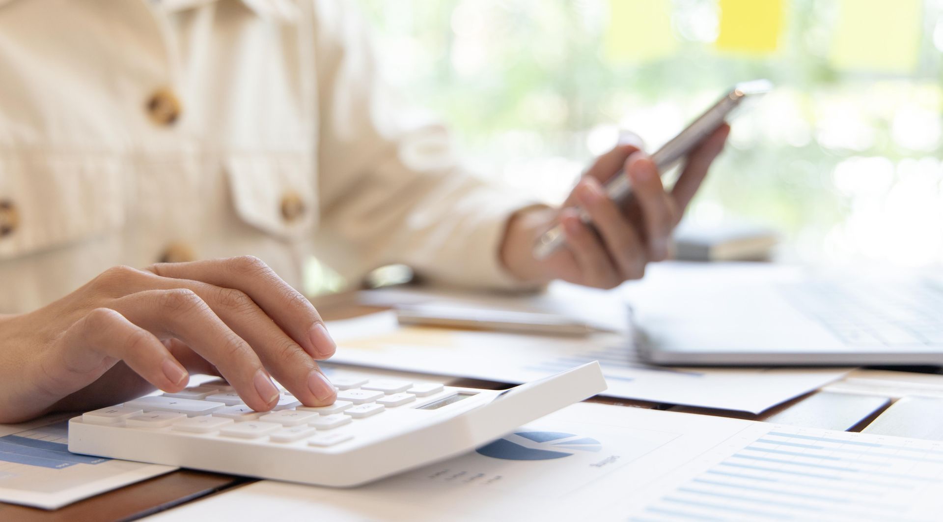 Person using a calculator and a smartphone while working at a desk, possibly on finances.