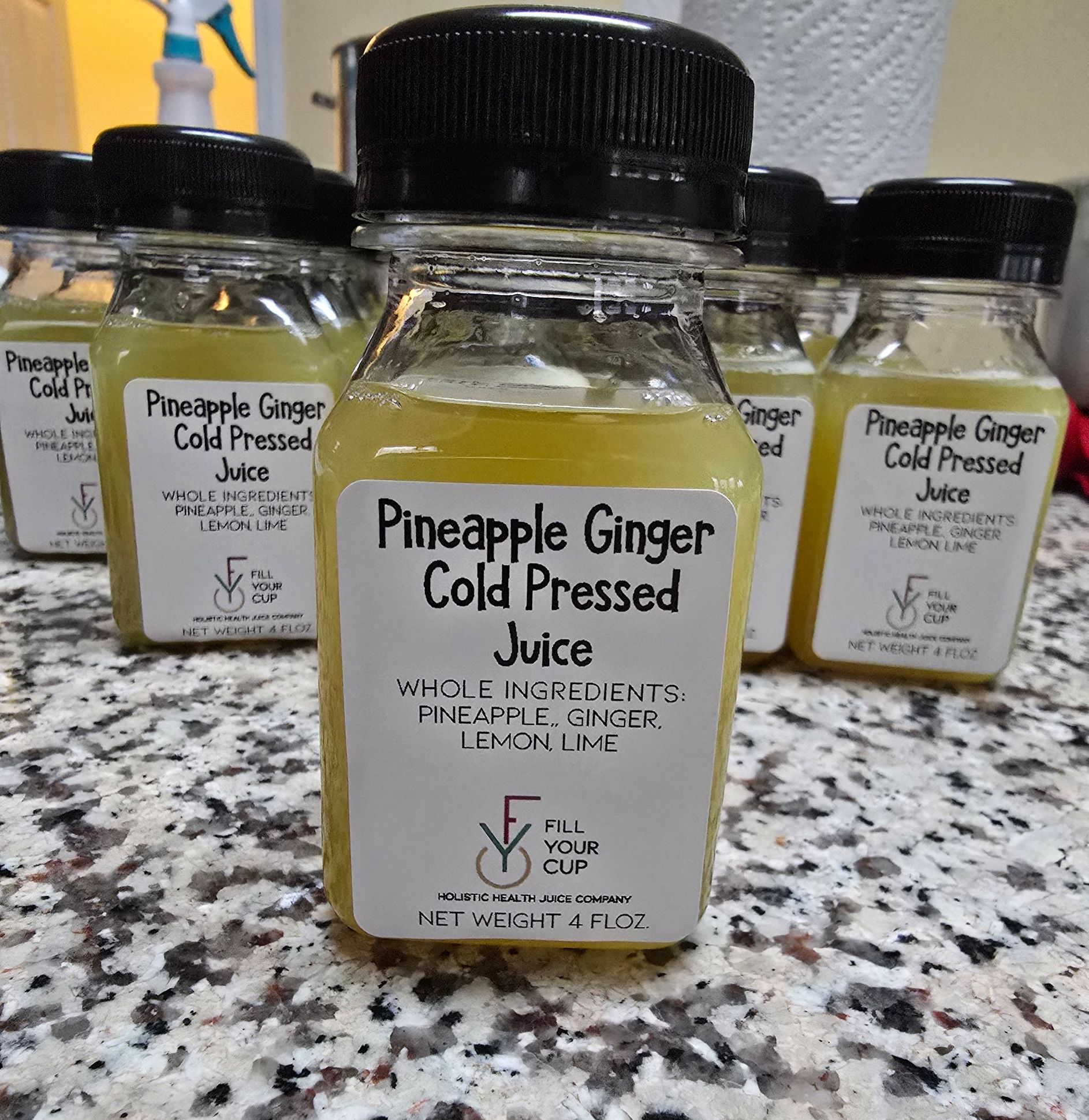 Bottles of Pineapple Ginger Cold Pressed Juice. Clear bottles, yellow liquid, black lids, labels.