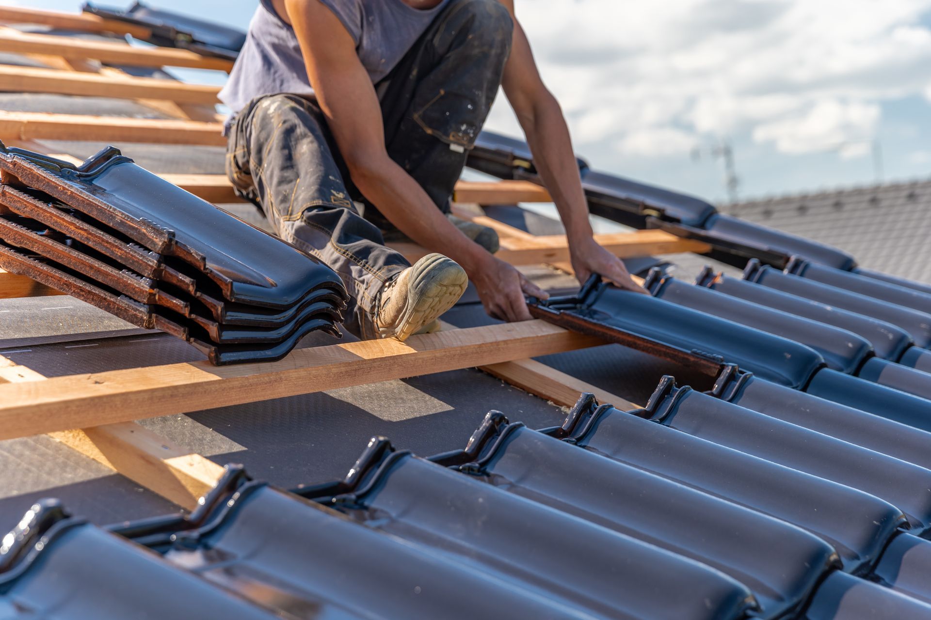 Worker installing gray roof tiles on a sloped roof