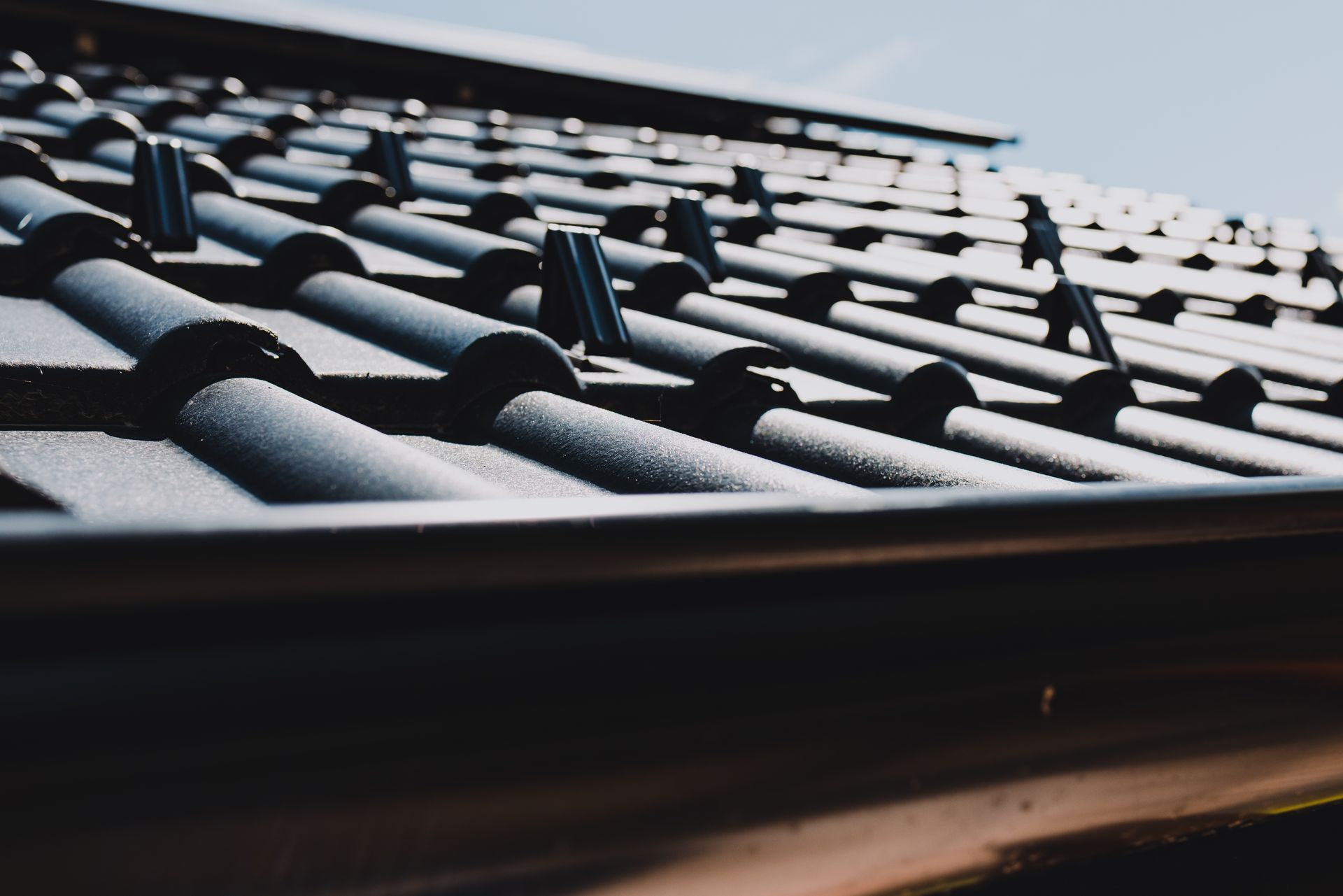 Close-up of dark roof tiles with sunlight reflecting on the sloped roofline