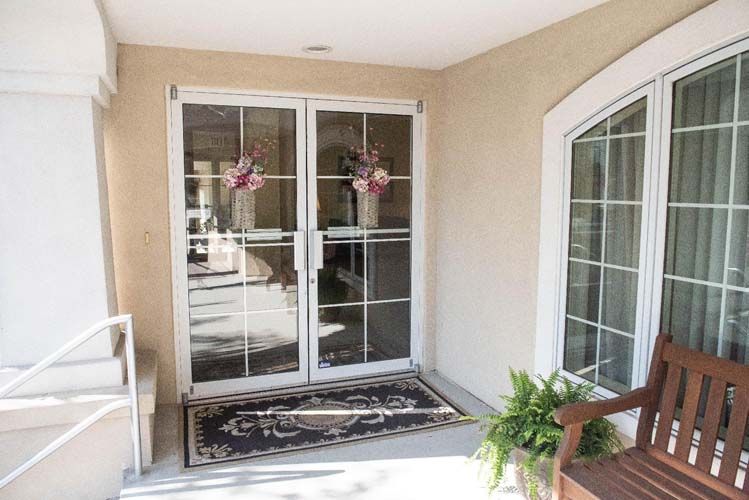 Glass doors with floral decorations lead into a building. A bench and plant are visible.