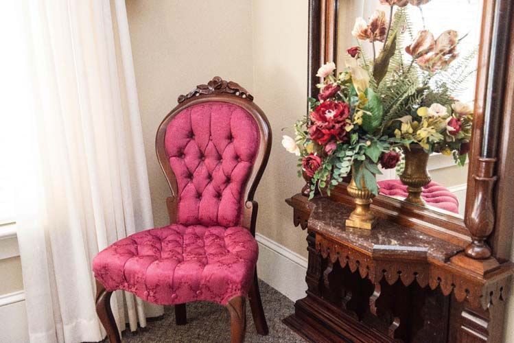 Burgundy upholstered chair next to a dark wood vanity with mirror and flowers.