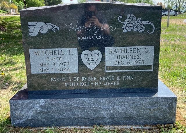 A black granite headstone for Mitchell T. and Kathleen G. Hertzler, featuring a Flyers logo, flower design, and text.