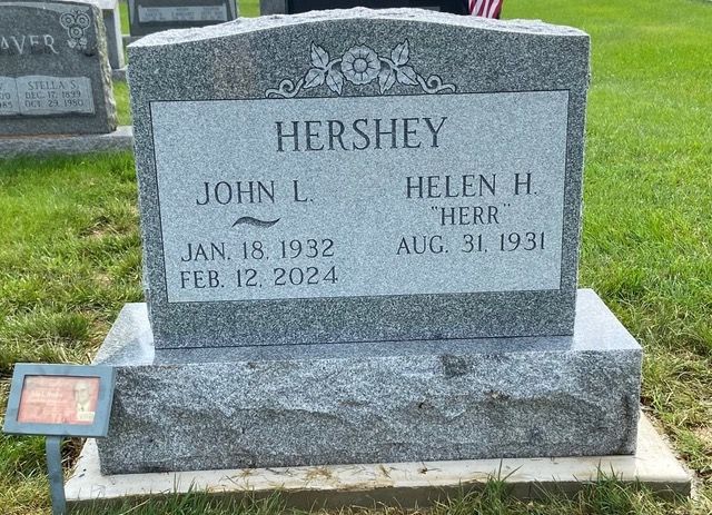 A gray granite gravestone for John L. (1932–2024) and Helen H. Herr Hershey (1931–), located in a grassy cemetery.