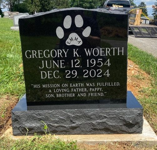 A black upright granite headstone for Gregory K. Woerth, featuring a paw print with