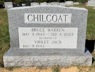 A gray granite headstone for Bruce Warren Chilcoat (1943–2024) and his wife, Violet Jack, in a cemetery.