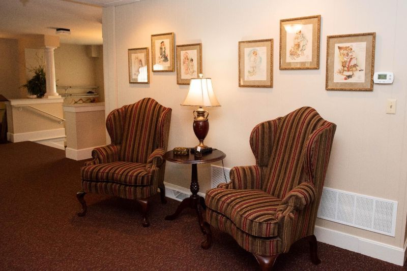Two wingback chairs with striped upholstery sit by a small table with a lamp; framed art hangs on the wall.