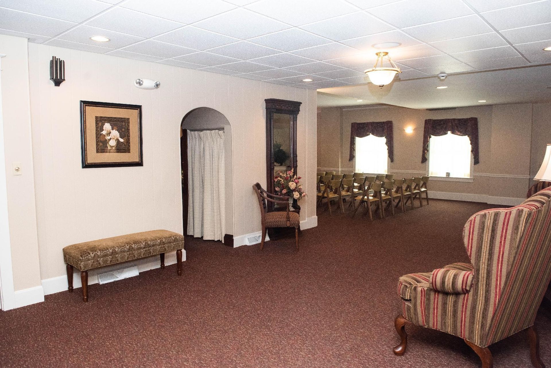 Interior of a room with chairs, an armchair, and an entryway. Brown carpet and light walls.