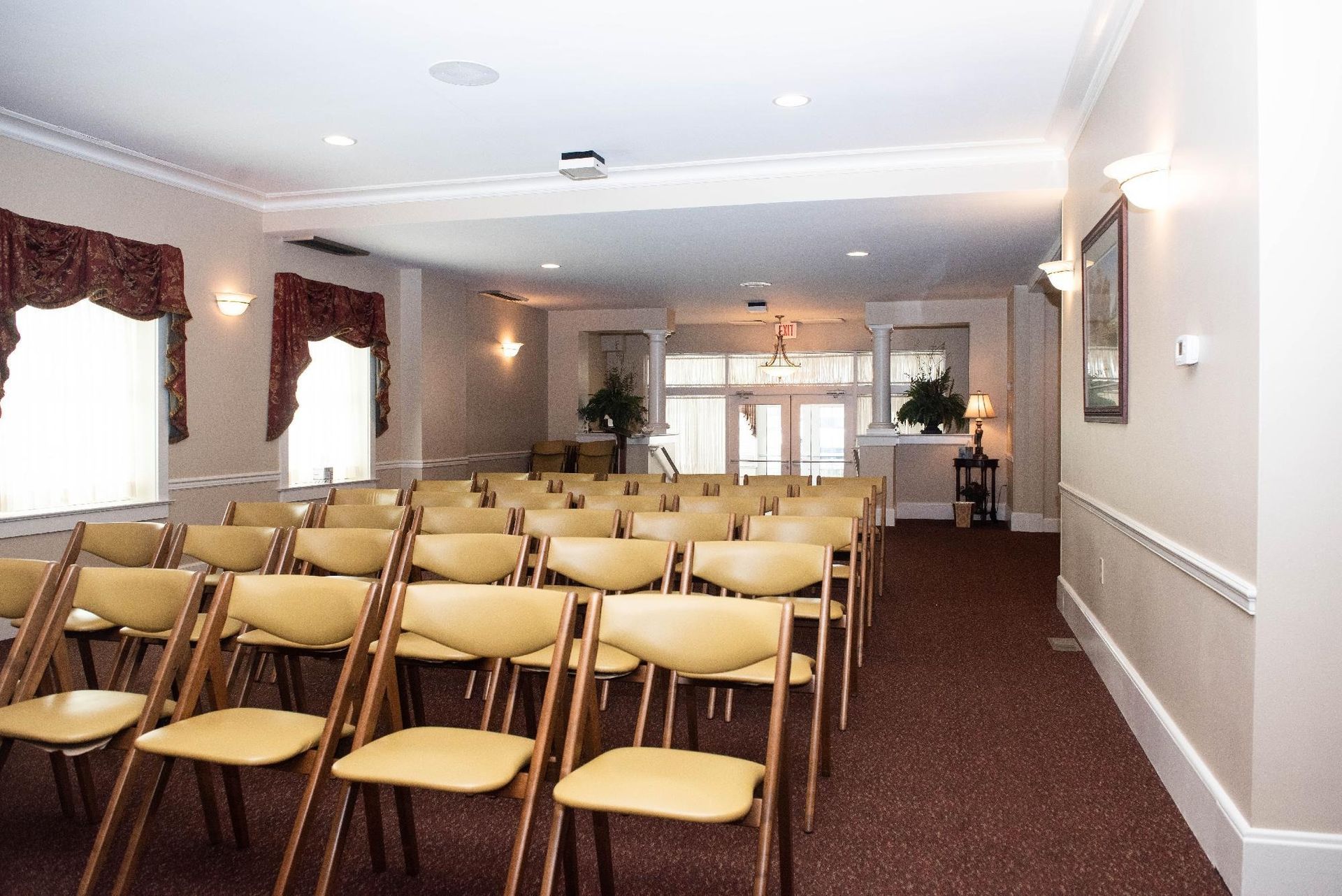 Rows of tan folding chairs face a doorway at the far end of an event space.