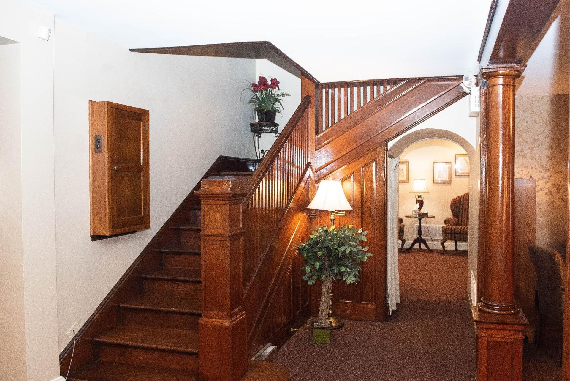 Wooden staircase with dark brown banister, leading to an upper level. Entryway with hallway and archway.