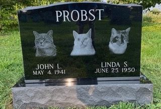 A black granite headstone with the name PROBST and the names and birth dates of John L. and Linda S. above three cat etched portraits.