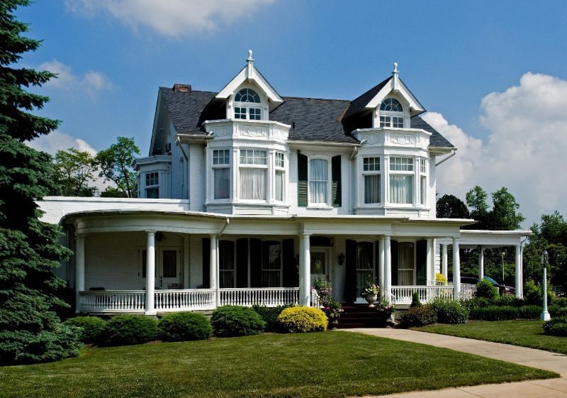 White Victorian house with porch, green lawn, and blue sky.
