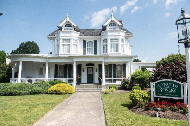 White Victorian house with porch, green shutters, and sign for Reynolds Seminary.